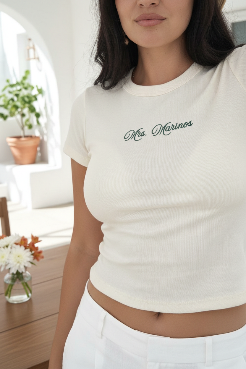 Model wearing a cream custom baby tee with Mrs. Marinos embroidery