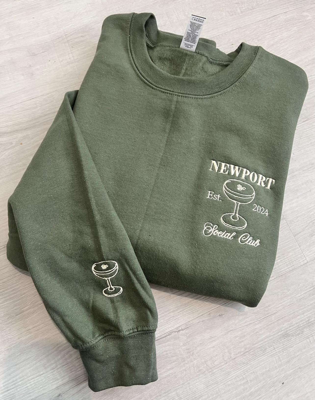 Folded green sweatshirt with Newport Social Club and sleeve embroidery
