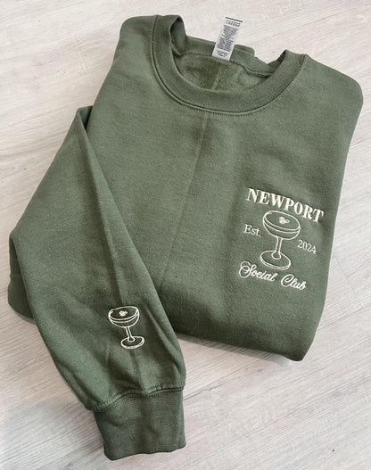 Folded green sweatshirt with Newport Social Club and sleeve embroidery