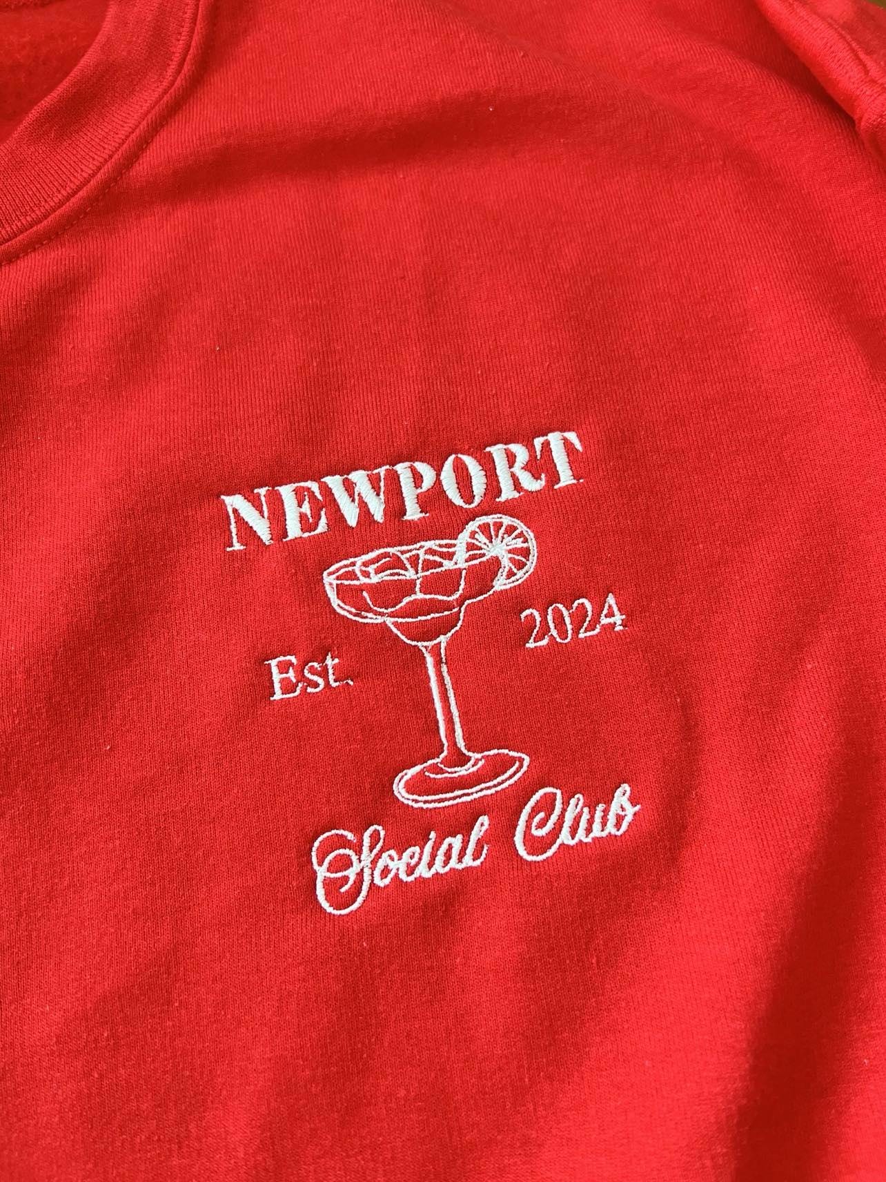 Close-up of white Newport Social Club embroidery on a red sweatshirt