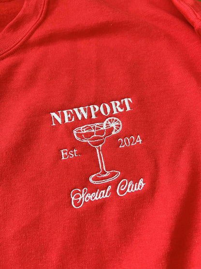 Close-up of white Newport Social Club embroidery on a red sweatshirt