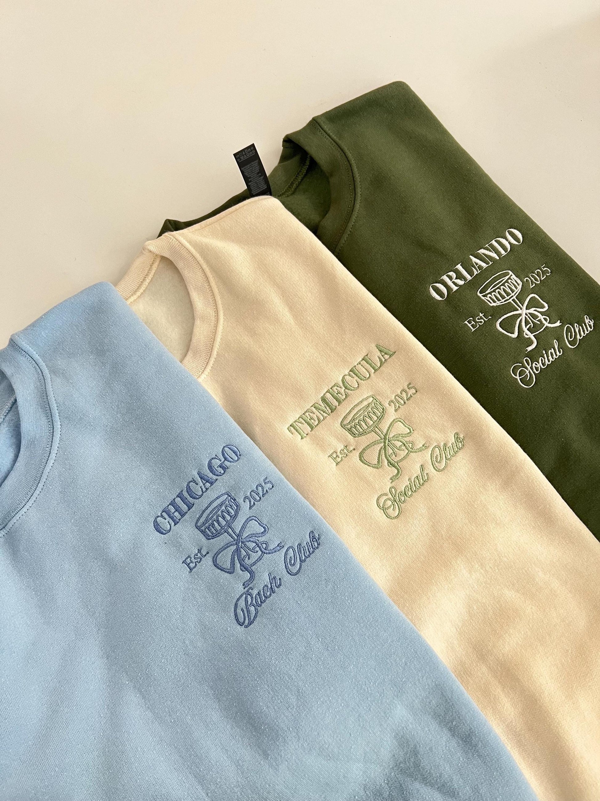 Three embroidered bridal party sweatshirts in blue, cream, and green