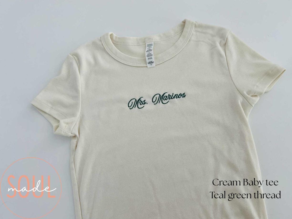 Cream baby tee with teal Mrs. Marinos embroidery
