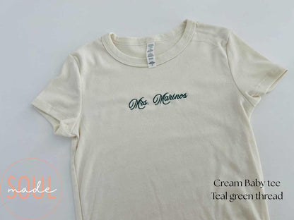 Cream baby tee with teal Mrs. Marinos embroidery