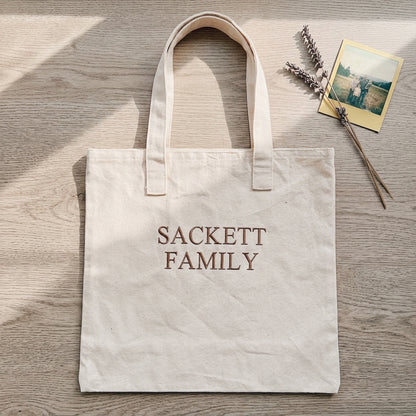Natural tote bag with Sackett Family embroidery on wood background