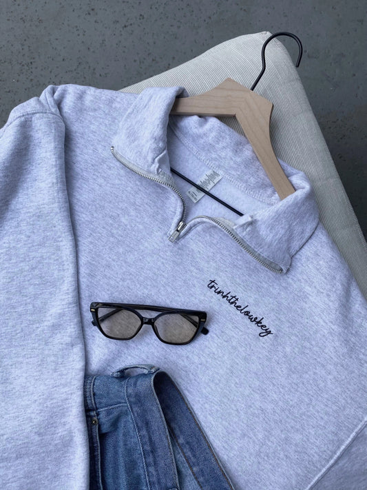 Gray quarter-zip sweatshirt on a hanger styled with sunglasses and jeans